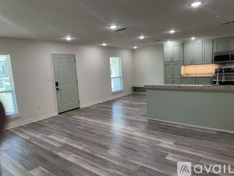 A spacious room with wooden flooring and a kitchen area in the background.