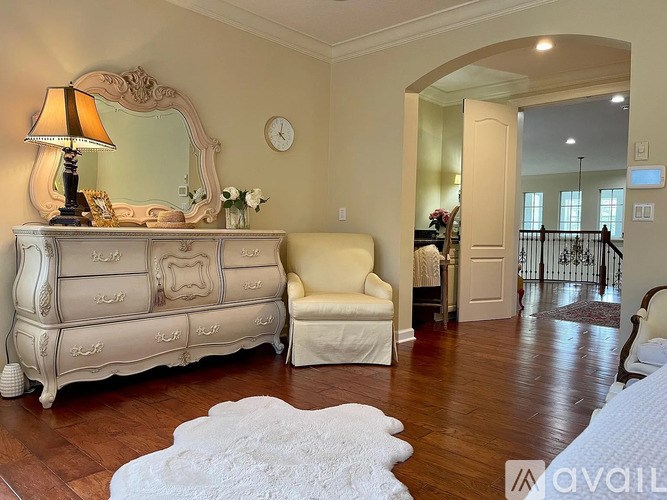 A bedroom with a large bed, a dresser, a chair, and a mirror.