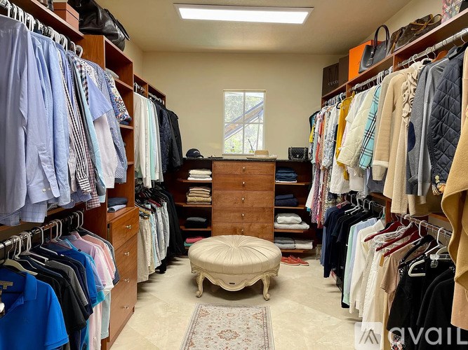 A walk in closet with a variety of clothes hanging on shelves and a bench in the middle.