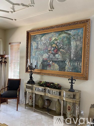 A large painting hangs above a console table with a black chair in front of it.