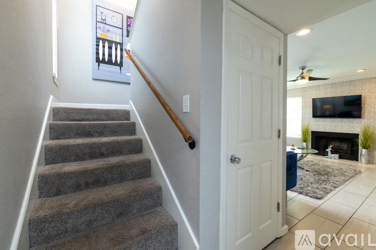 A staircase with a carpeted runner and a wooden handrail leads to a living room with a fireplace and a television.