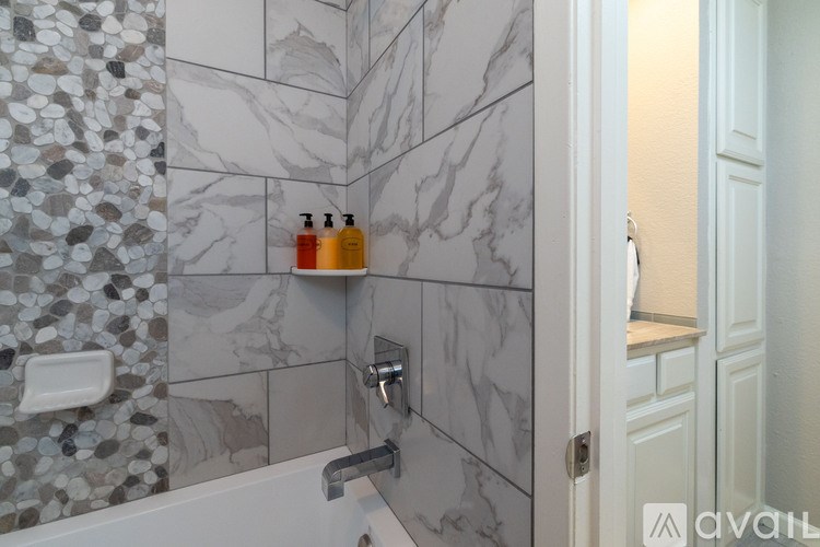 A bathroom with a marble tile wall and a white bathtub.