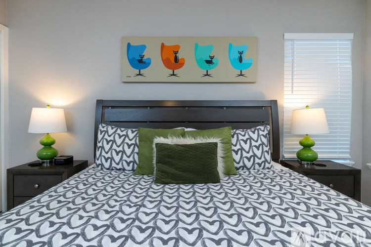 A bed with a patterned comforter and a green pillow is flanked by two nightstands with lamps.