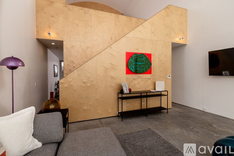 A living room with a grey couch, a purple lamp, a wooden table, and a green painting on the wall.