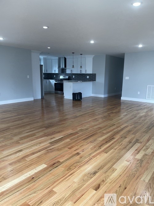 A spacious room with wooden flooring and a kitchen area in the background.