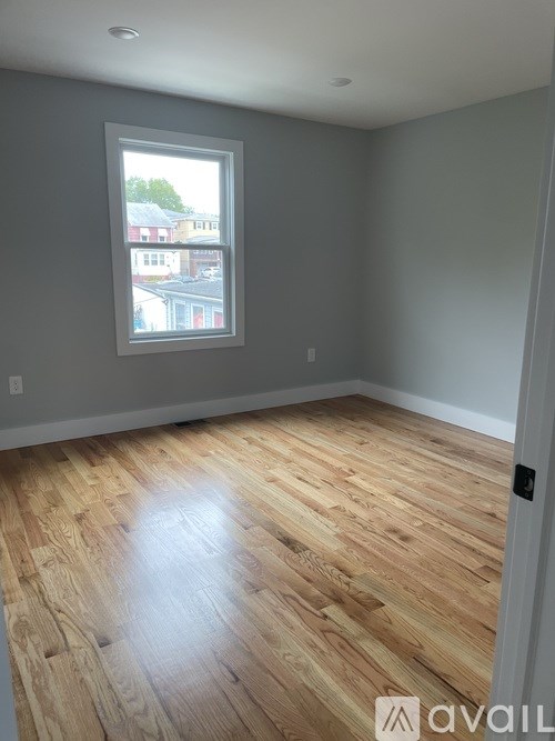 A room with wooden flooring and a window showing a view of buildings outside.