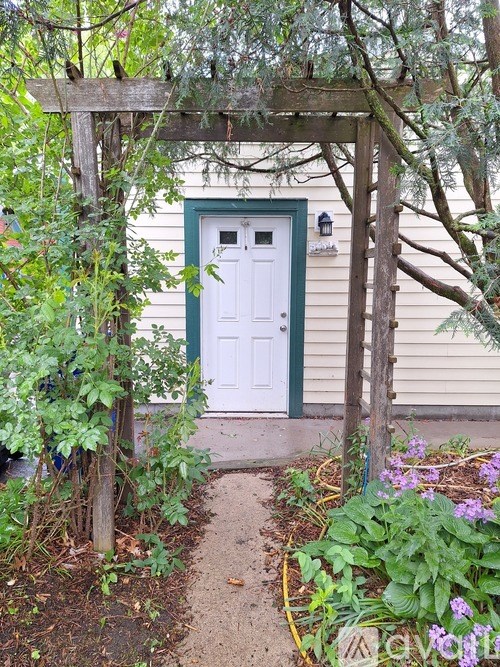 A white door with a green frame is surrounded by plants and flowers.