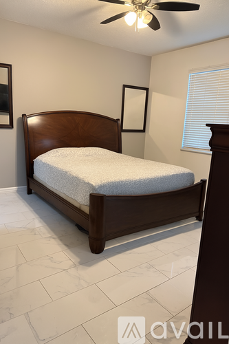 A bedroom with a bed, a ceiling fan, and a window with blinds.
