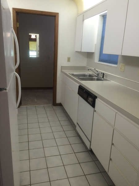 A kitchen with white cabinets and a black trash can.