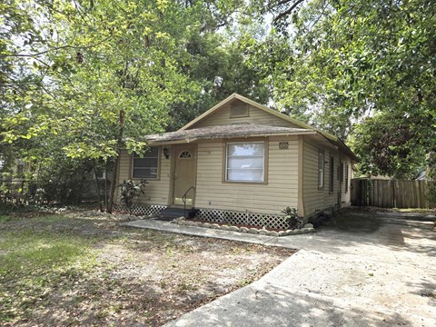 A small house with a porch is surrounded by trees.
