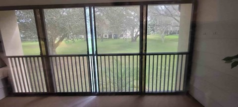 A balcony with a view of a green lawn and trees.