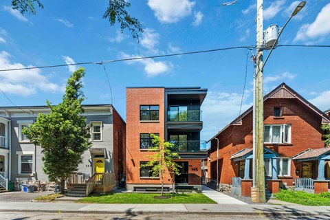 A modern red brick house with a glass balcony is in front of a row of older houses.