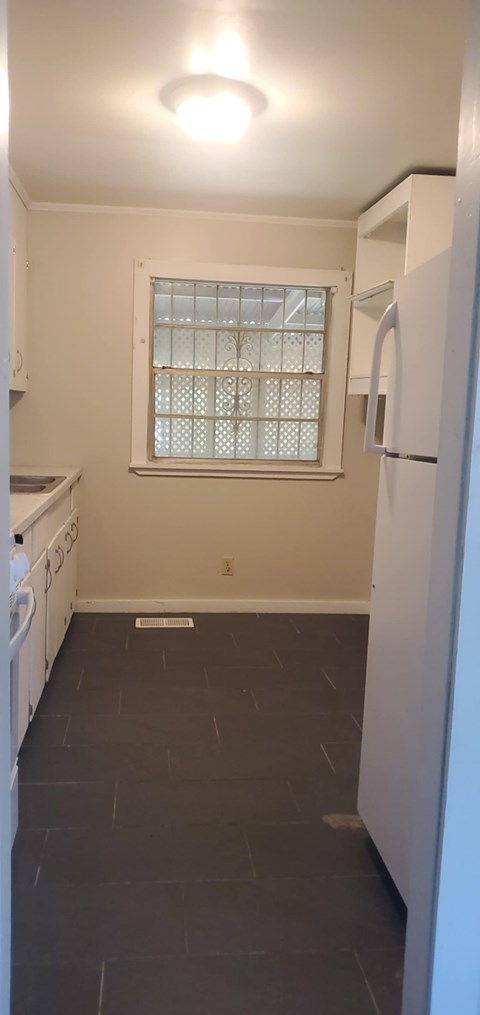 A kitchen with a white fridge and a window with blinds.