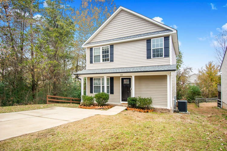 A house with a grey siding and a black door is surrounded by a grassy area and trees.