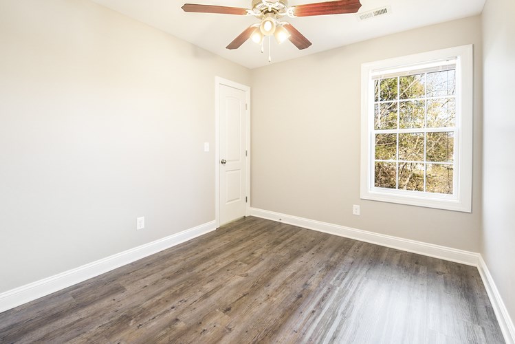 A room with a ceiling fan and a window with a view of trees.