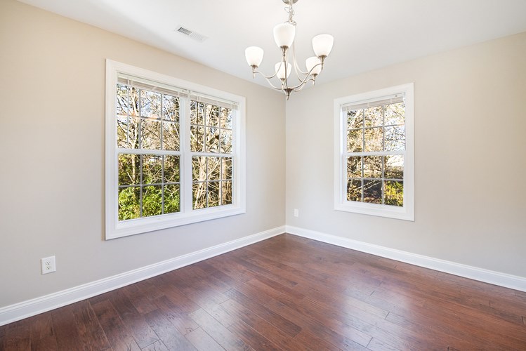 A room with a chandelier, two windows, and hardwood floors.