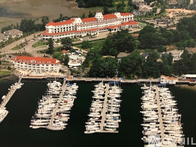 A large white building with a red roof sits next to a marina filled with boats.