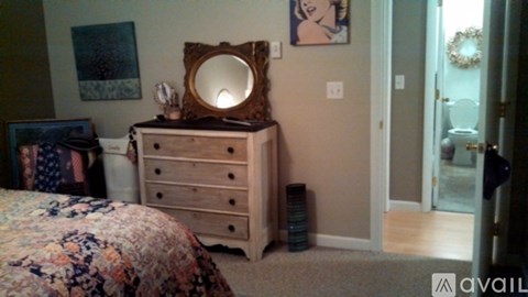 A wooden dresser with a mirror on top is in a room with a bed and a doorway leading to another room.