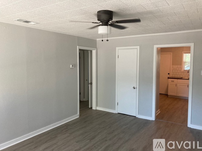 A room with a ceiling fan and a door leading to a kitchen.