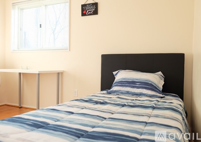 A bed with blue and white striped bedding sits in a room with a white table and a window.