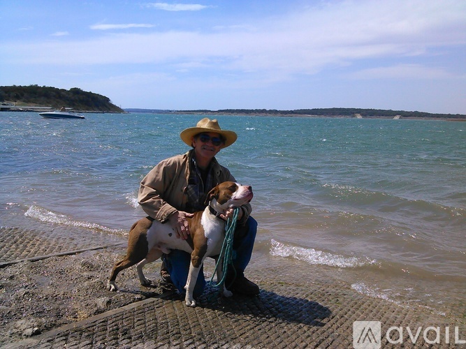 A man in a hat and jacket is kneeling down with a dog on a leash.