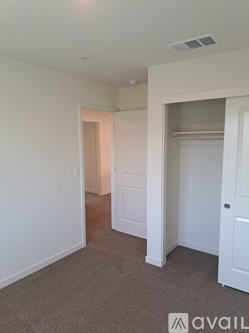 A room with white walls and carpeted floor with a door on the right.