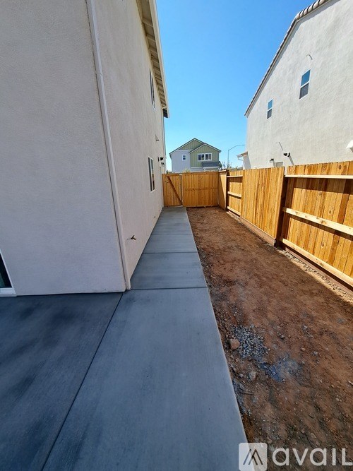 A long concrete walkway leads to a white building with a wooden fence on the right.