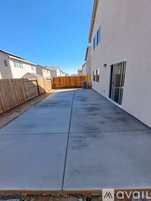A concrete driveway leads to a white house with a wooden fence on the side.