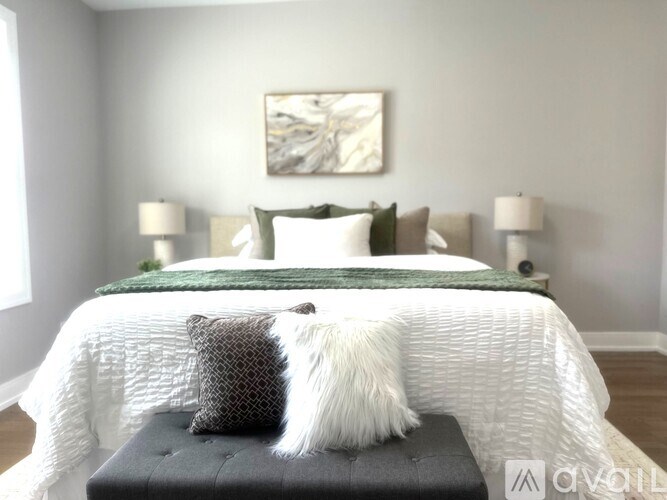 A white bed with a green pillow and a white dog on a black ottoman.