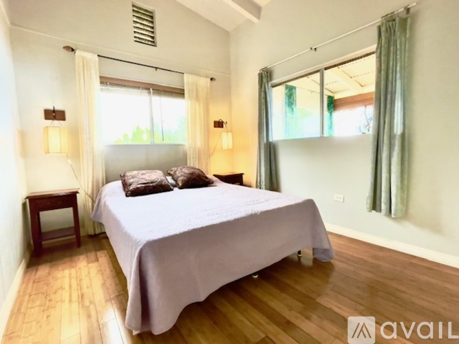 A bedroom with a bed, two lamps, and a window with curtains.