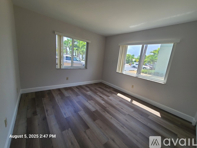A room with wooden flooring and two windows showing a view of a street.