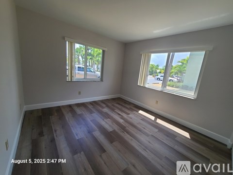 A room with wooden flooring and two windows showing a view of a street.