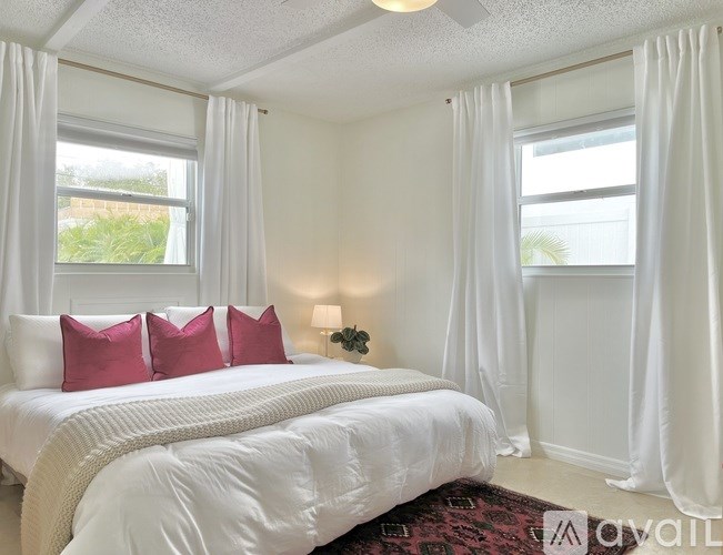 A bedroom with a large bed and two windows with white curtains.