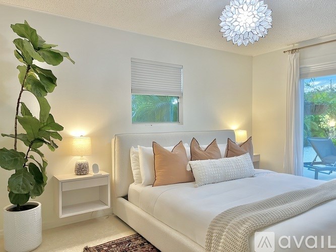A bedroom with a large bed, a potted plant, and a window with blinds.