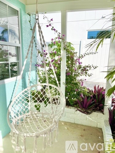 A white hanging chair with a plant in it is in front of a window.