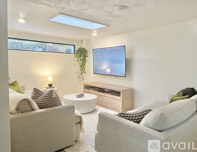 A living room with a grey couch, a white coffee table, and a flat screen TV mounted on the wall.