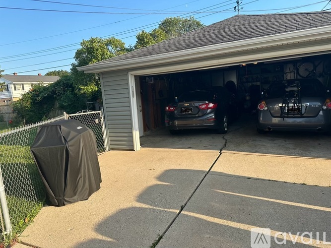 A garage with two cars and a grill in the driveway.