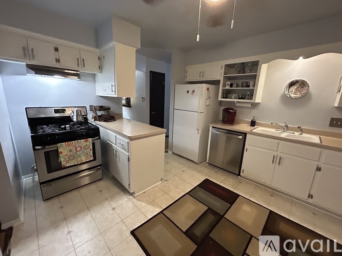 A kitchen with white cabinets and appliances, a rug on the floor, and a ceiling fan.