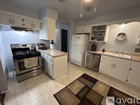 A kitchen with white cabinets and appliances, a rug on the floor, and a ceiling fan.