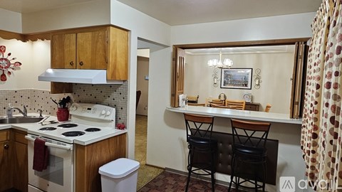 A kitchen with a white stove top oven and a white trash can.