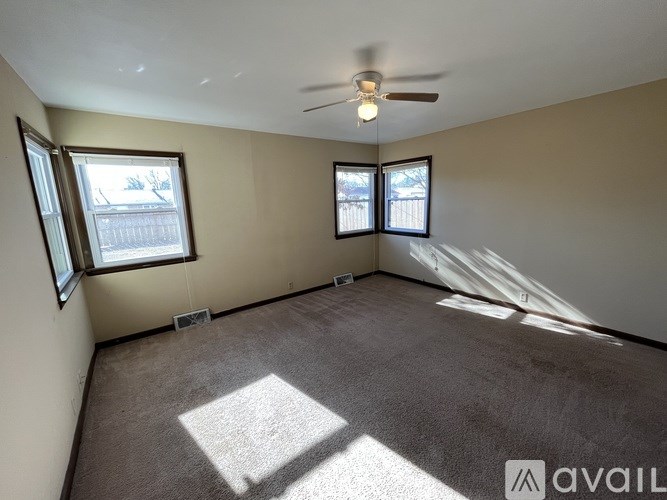 A room with a carpeted floor, a ceiling fan, and two windows.