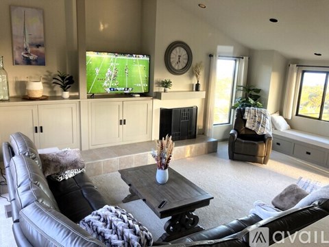 A living room with a leather couch, a coffee table, and a television playing a football game.