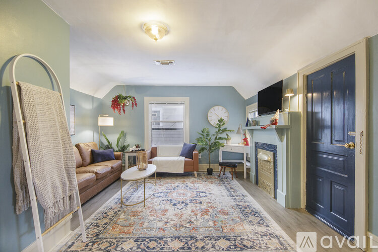 A living room with a rug, a sofa, a chair, a table, a plant, a clock, a window, a door, and a wall hanging.