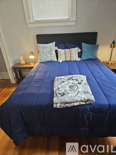 A bedroom with a bed, a chair, and a table with a lamp on it.