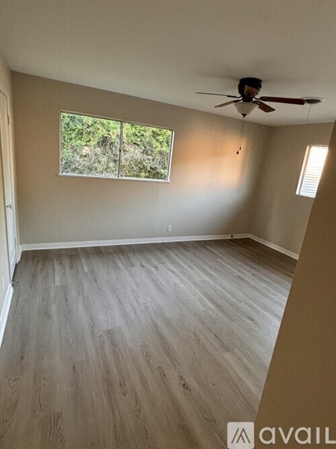 A room with a ceiling fan and a window with a view of trees.