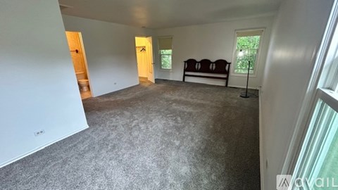A spacious living room with a grey carpet and a white wall.