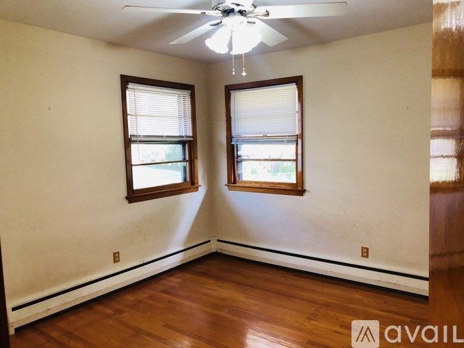 A room with a ceiling fan and two windows.