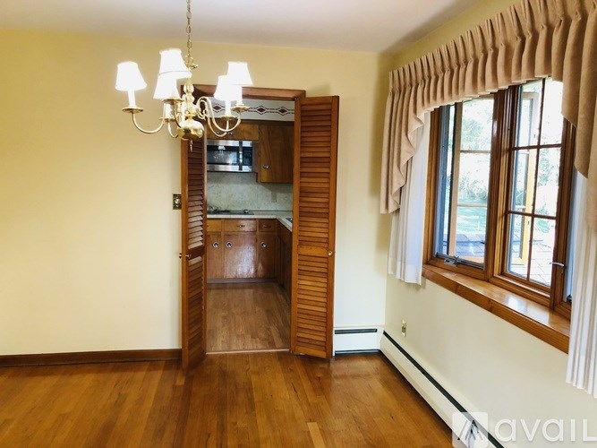 A room with a chandelier, wooden floors, and a window with curtains.