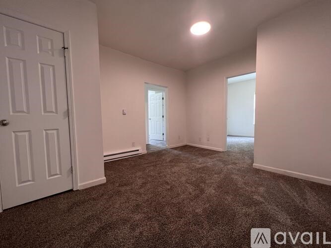 A room with carpeted floor and white walls, with a door on the left and a window on the right.