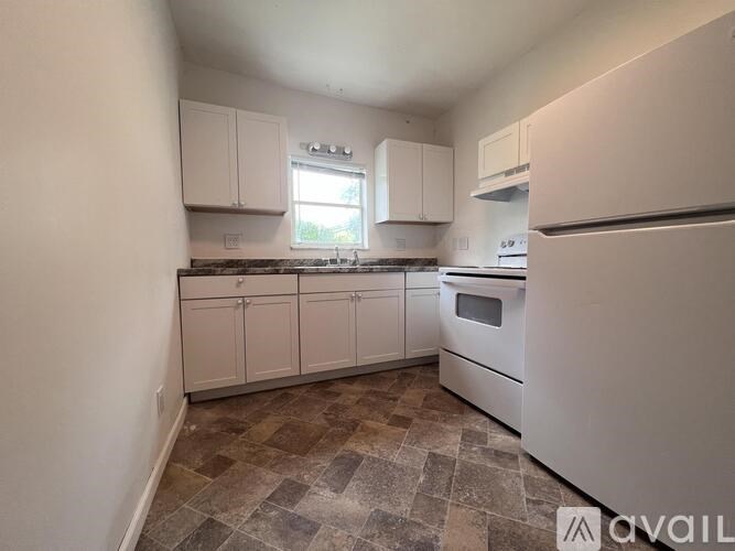 A kitchen with white appliances and cabinets, and a tiled floor.